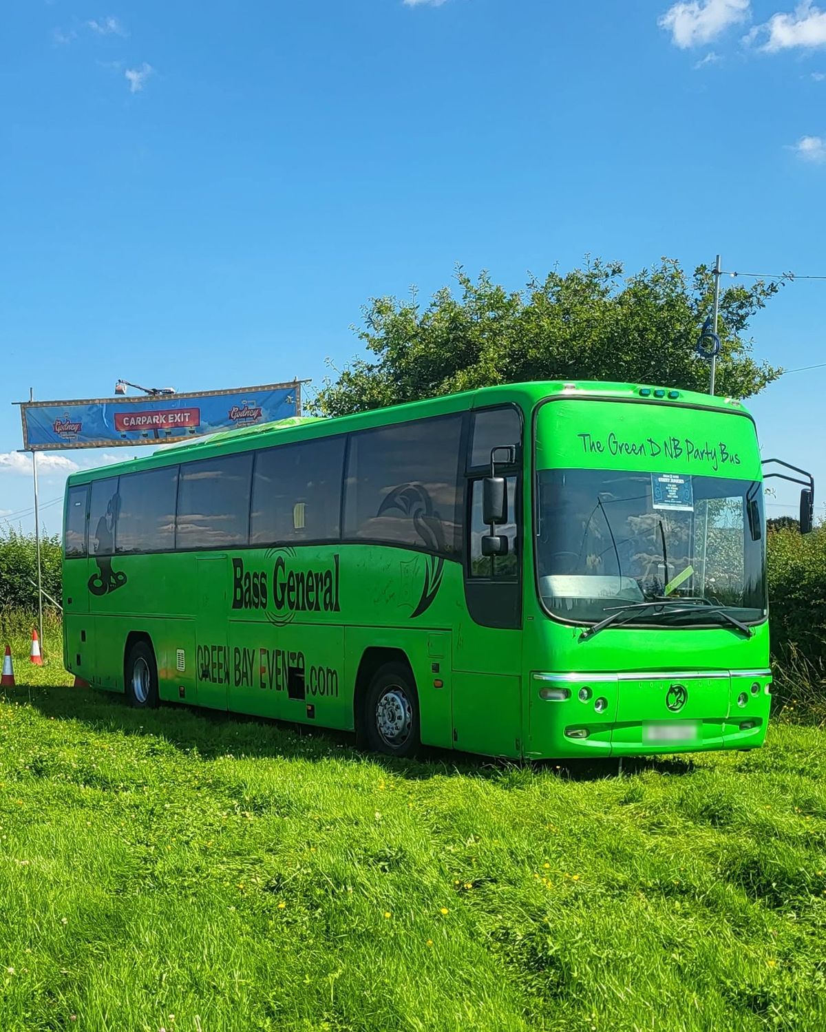 The green coach parked on a festival field under a blue sky